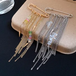 Detail of safety pin brooches featuring dangling tassel chains and natural stone accents