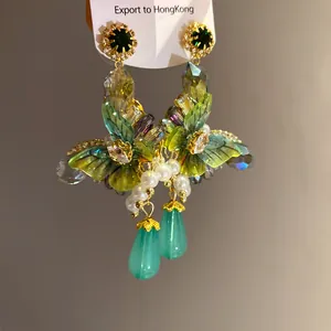 Close-up of forest style flower earrings with zircons, pearls, and green drops.