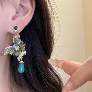 Detailed view of iridescent butterfly drop earrings with pearls and green zircon studs