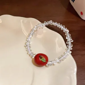 Close-up of clear beaded resin bracelet featuring a red apple pendant on a ceramic plate
