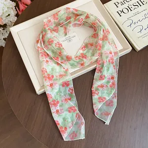 Detailed macro shot of a green floral silk scarf with vibrant orange patterns on a tray.