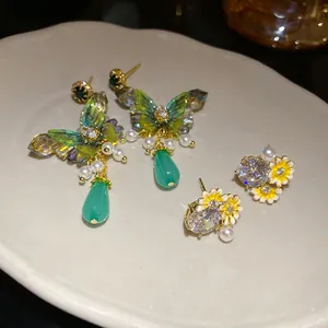 Close-up of elegant butterfly drop earrings and daisy studs with green and yellow accents