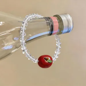 Close-up detail of a charming red apple pendant on a clear beaded resin bracelet accessory