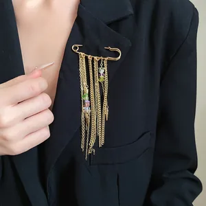 Close-up of vintage gold safety pin brooch with colorful stone tassel chains on a black blazer
