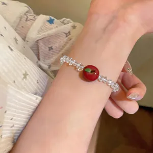 Close-up detail of a sweet red apple pendant on a clear heart-beaded bracelet.