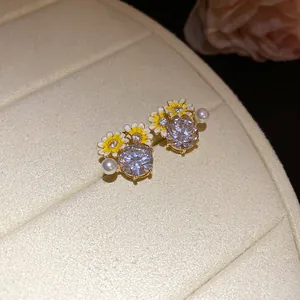 Detailed macro view of gold-tone zircon earrings featuring enamel daisies and pearls