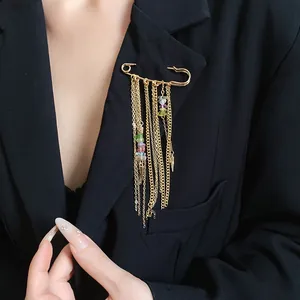 Detail view of gold safety pin brooch with chain tassels and colorful stones on blazer