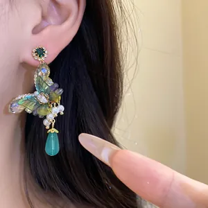 Close-up of forest-style butterfly earrings featuring green crystals and pearl pendants