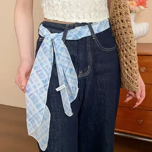Detail of a blue checkered floral scarf styled as a waist belt on denim jeans