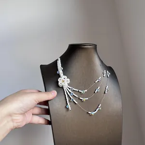 Detail view of a white multi-layer beaded necklace with flower and tassel charms