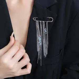 Detail view of a silver safety pin brooch with hanging chains and blue stones on a blazer.