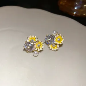 Close-up detail of silver pin stud earrings with yellow enamel flowers and cubic zirconia