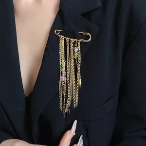 Detailed view of a gold safety pin brooch with long chain tassels and colored stones