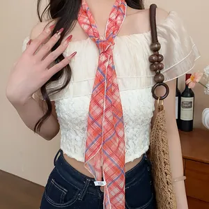 Detail view of a red plaid skinny scarf necklace styled with a cream lace top