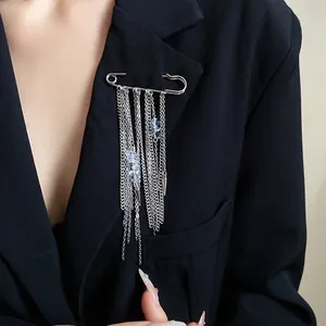 Close-up of a silver safety pin brooch with hanging chains and light blue stones on a blazer.