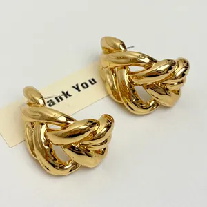 Close-up detail of chunky gold-plated twisted C-shape hoop earrings with hollow design