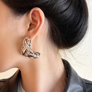 Close-up of chunky silver C-shaped chain link hoop earrings worn on a model's ear