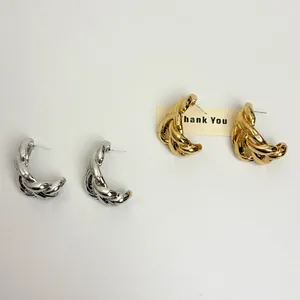 Detail view of silver and gold C-shaped twisted chain stud earrings on plain surface