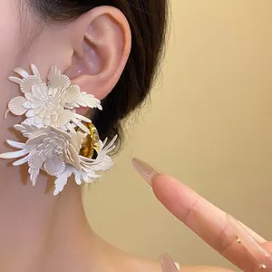 Elegant white leather flower C-shaped stud earrings with gold center worn by model
