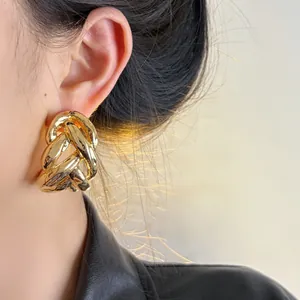 Macro view of chunky gold-tone interwoven chain link stud earring worn by model