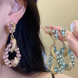 Detailed close-up of crystal-encrusted feather drop earrings in pink and blue tones.