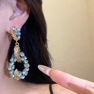 Close-up of elegant blue rhinestone teardrop earrings with golden feather accents
