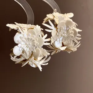 Close-up view of elegant cream leather flower C-shaped earrings with pearl accents.