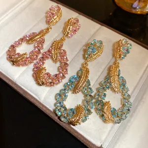 Close-up of elegant gold feather teardrop earrings with pink and blue stones