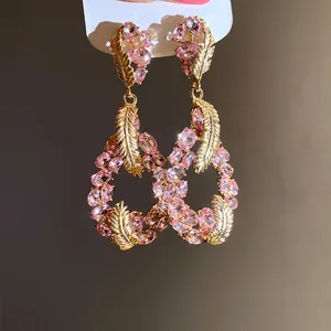 Close-up detail of pink gemstone drop earrings with golden feather design accents.