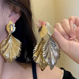 Detailed close-up shot of large metallic leaf earrings with a unique wrinkled texture