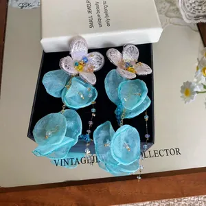 Close-up of blue chiffon flower earrings with long beaded tassels in a jewelry box