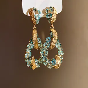Detailed view of ornate gold feather earrings with light blue crystal clusters