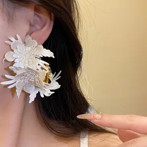 Macro detail of large cream leather flower C-shaped earrings worn by a model