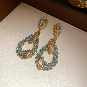 Detailed view of elegant gold feather water drop earrings with blue gemstones and stones.
