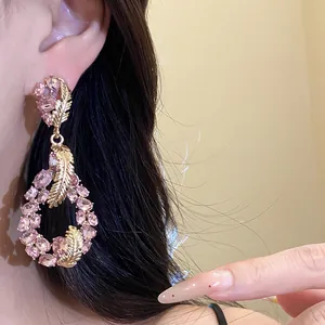 Close-up detail of silver needle drop earrings with pink crystals and gold feathers