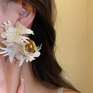 Close-up view of vintage-style ivory leather flower C-shaped earrings with gold accents.
