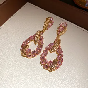 Elegant gold-tone feather teardrop earrings with sparkling pink oval crystals close-up.