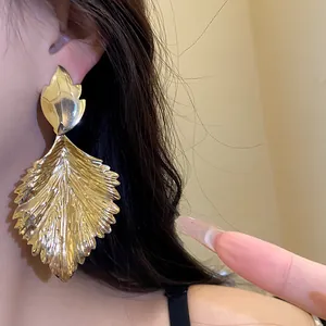 Macro detail of large golden metallic leaf earrings featuring a unique crumpled texture