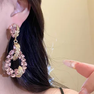 Close-up of pink crystal feather drop earrings with elegant gold-tone metal finish.