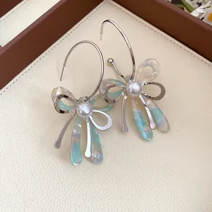 Detailansicht eleganter Schleifenohrringe mit buntem Marmordesign und weißer Perle