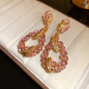 Detailed view of pink crystal earrings with gold feather accents in waterdrop shape