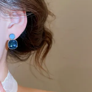 Detailed view of elegant square blue crystal drop earrings worn on a model's ear