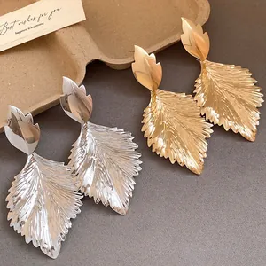 Close-up of metallic pleated leaf drop earrings with intricate texture in gold and silver.
