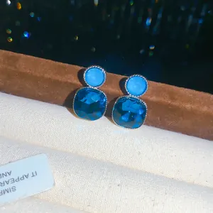 Close-up of elegant blue square crystal stud earrings with silver-toned border details.