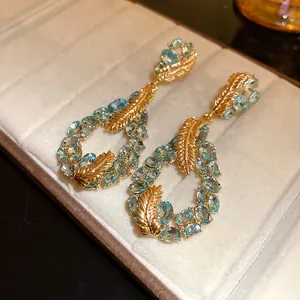 Exquisite detail of golden feather teardrop earrings featuring light blue oval crystal stones