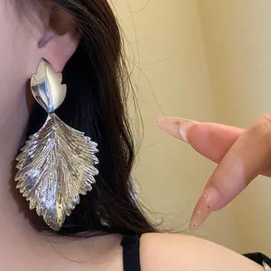 Close-up of a large metallic wrinkled leaf earring worn on a model's ear