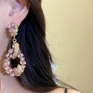 Close-up of elegant pink crystal teardrop earrings with gold feather design details