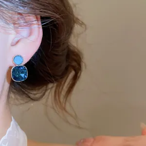 Close-up of elegant blue crystal square stud earrings with small round top worn on ear