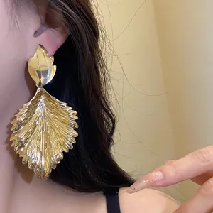 Close-up of large golden metallic leaf drop earrings with detailed vein textures.
