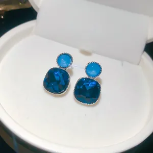 Close-up view of elegant square blue crystal stud earrings presented in a white jewelry box.